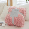 A pink plush throw blanket with a quilted pattern is presented on a white cushion.