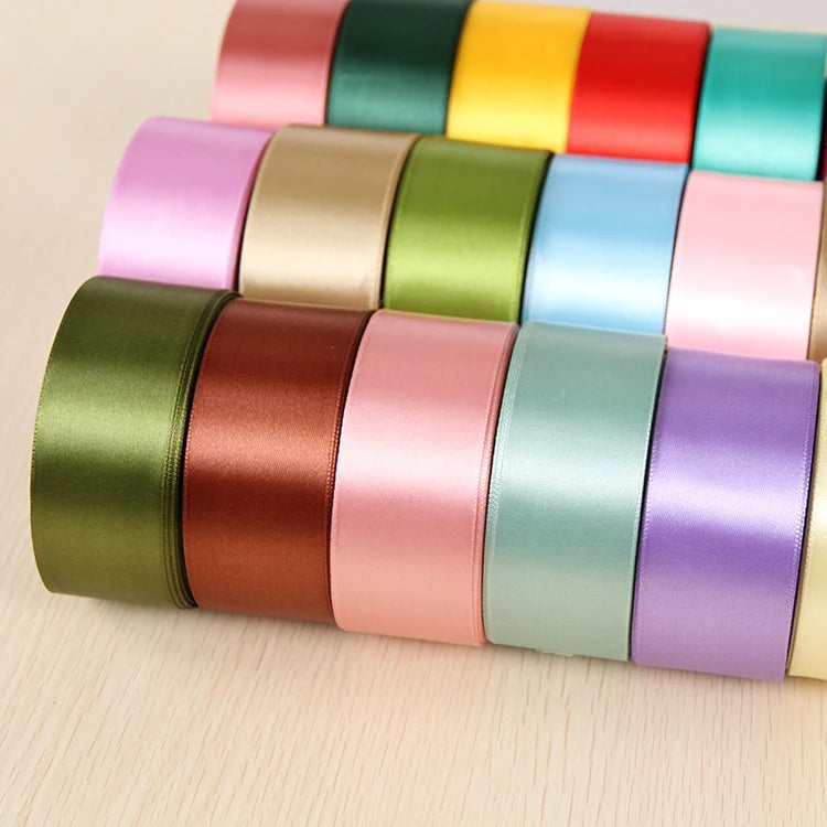 A collection of colorful satin ribbon rolls in various shades of pink, green, yellow, and purple arranged in a row.