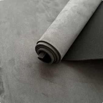 Roll of gray suede auto headliner fabric with foam backing lying on a dark surface.