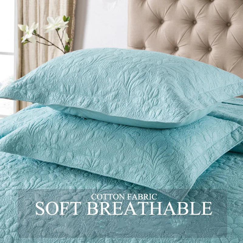 Light blue quilted cotton pillow covers stacked on a bed with a beige headboard.