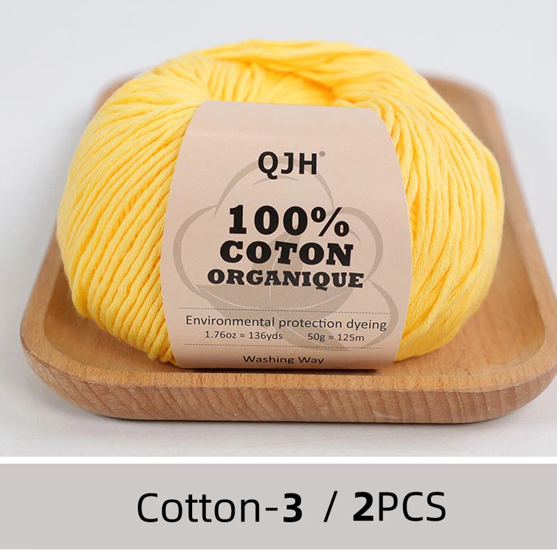 A ball of bright yellow 100% organic cotton yarn for knitting and crochet displayed on a wooden tray.
