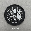A black embroidered patch featuring a white medical cross design with an eye motif on a gray background.
