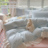 A set of light blue and white gingham duvet cover and pillowcases with a fluffy teddy bear toy.