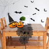 A wooden table set for Halloween featuring a black lace spider web table runner and decorative bats on the wall.