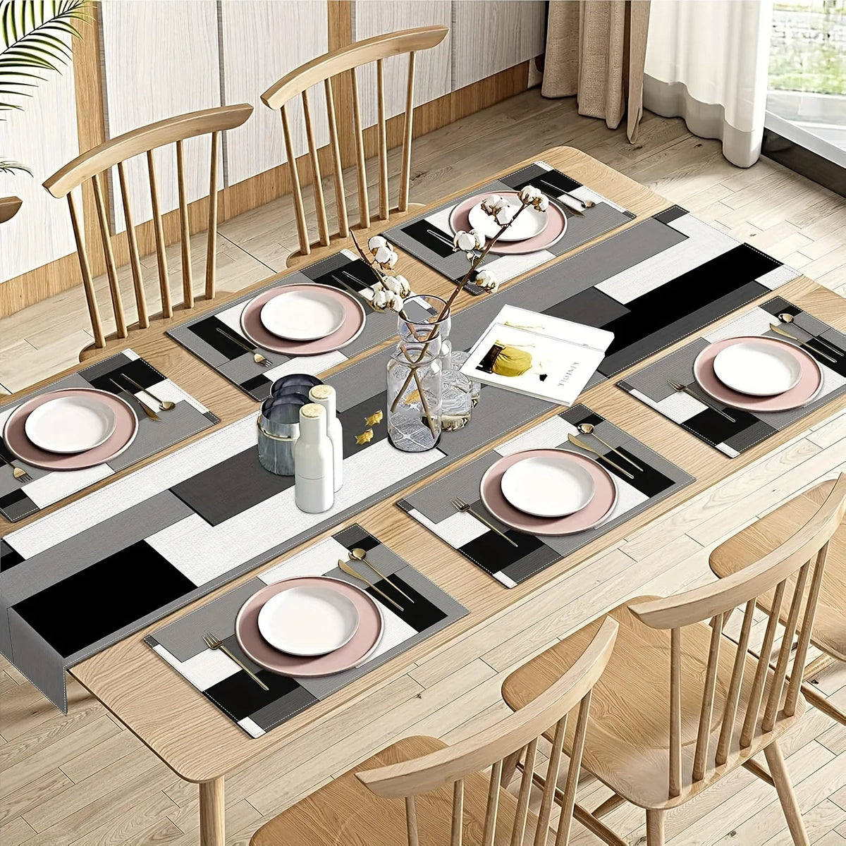 A modern geometric placemat set for dining featuring black, white, and gray patterns with small white floral accents.