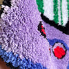 Close-up of a purple tufted floor mat with black and green stripes and colorful embroidered designs.
