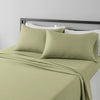 A set of four olive green microfiber flat fitted sheets on a bed with white pillows and a gray headboard.
