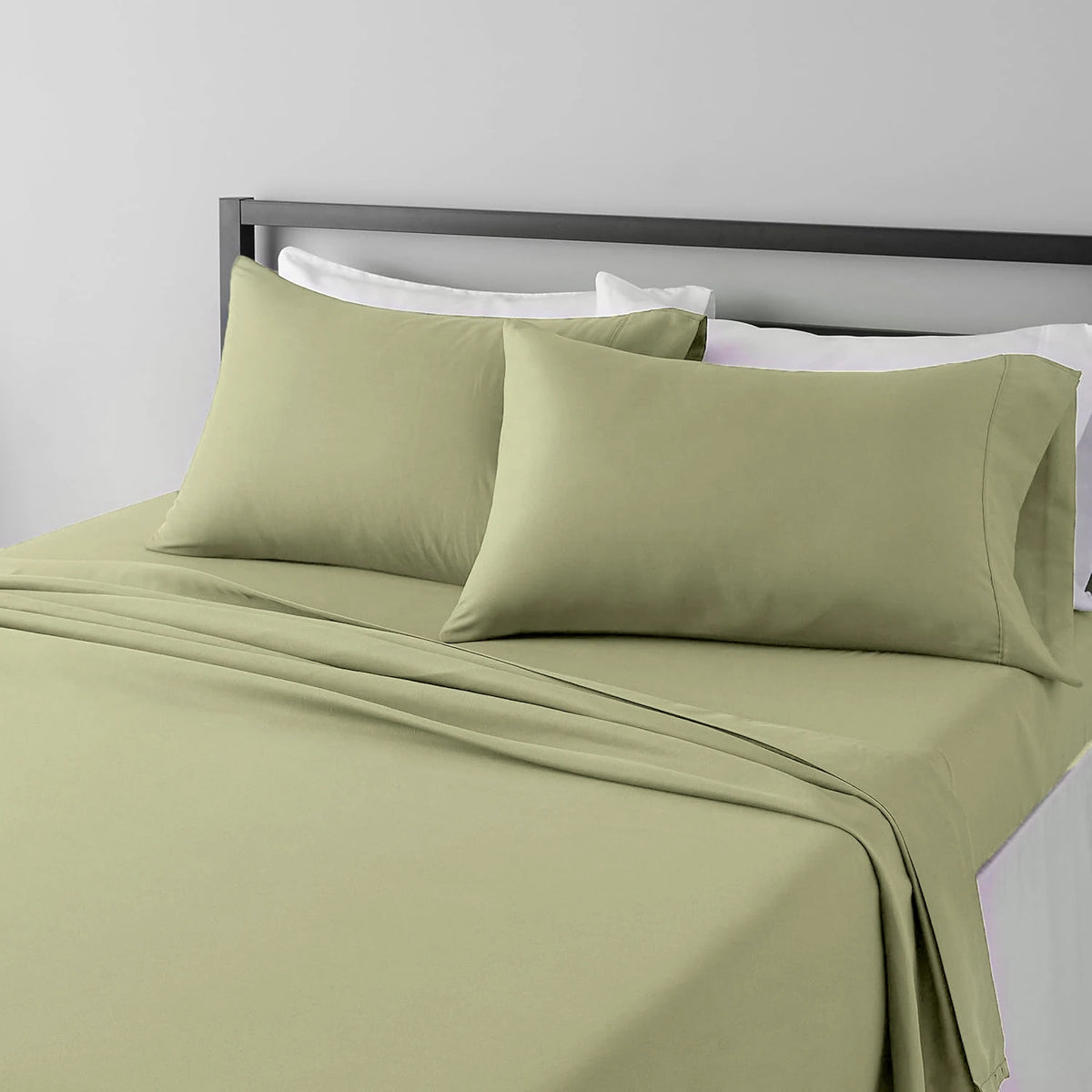 A set of four olive green microfiber flat fitted sheets on a bed with white pillows and a gray headboard.