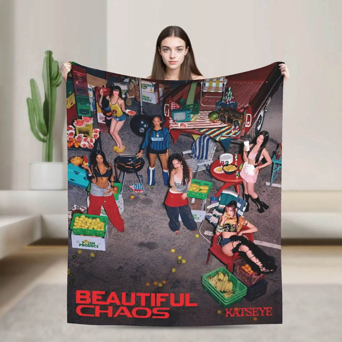 A person holds up a large blanket featuring a chaotic scene with people and objects, titled Beautiful Chaos.