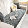 A thick gray flannel sofa pad cover with a white flower pillow and a small white teacup on a white sofa.