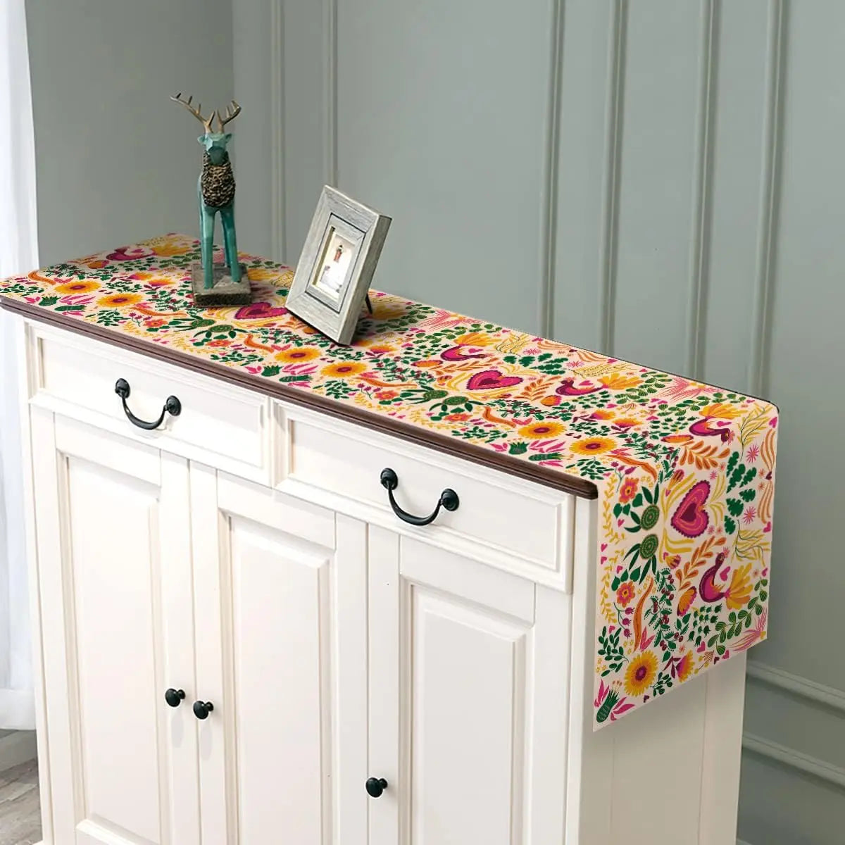 A linen table runner featuring colorful Day of the Dead floral pattern displayed on a white cabinet.