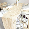 A long, flowing beige gauze table runner draped elegantly on a white tablecloth for a wedding or elegant decoration.