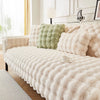 A beige plush rabbit fur sofa cushion cover with a green accent cushion on a light-colored sofa.