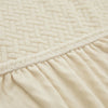 Close-up of a beige quilted fabric sofa cover with a gathered hemline.