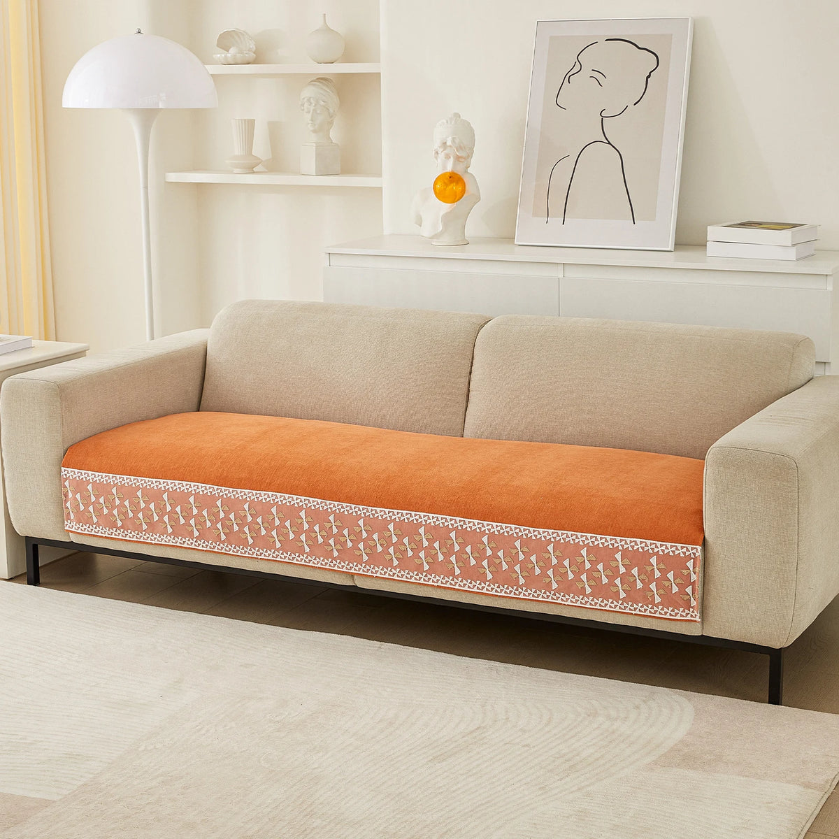 A beige sofa with an orange quilted cover featuring a white lace trim, set in a bright living room.