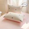 A set of three white pillows with black bowknot embroidery displayed on a pink surface.