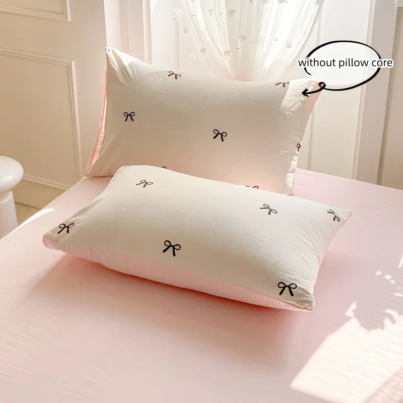 A set of three white pillows with black bowknot embroidery displayed on a pink surface.