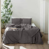 A gray luxury French linen duvet cover is displayed on a bed with white linens and a large green plant in the background.