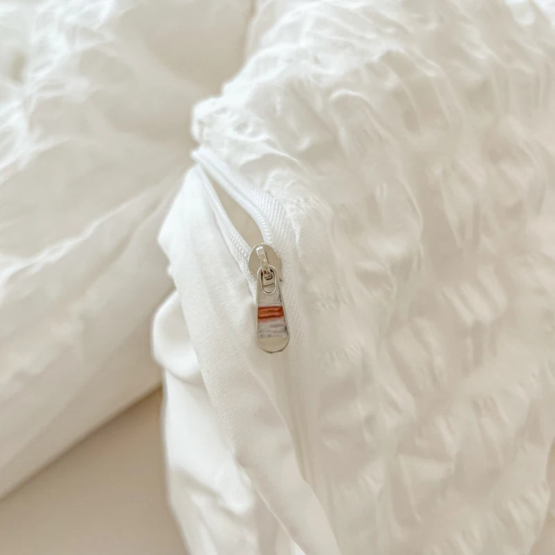 Close-up of a white seersucker duvet cover and pillow set with a silver zipper detail.