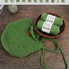A hand-knitted green mesh face mask is shown next to two rolls of green hollow cotton yarn.