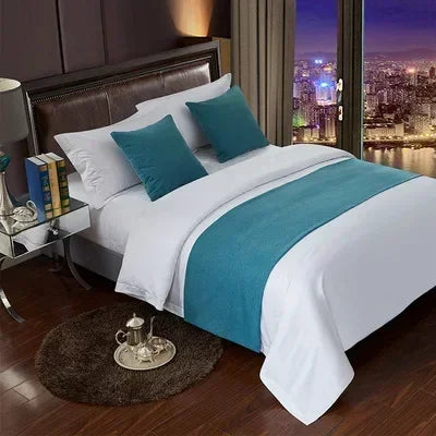 A luxurious bedroom featuring a bed with white linens and teal accents, next to a large window view of a city skyline.
