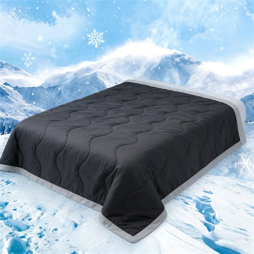 A dark gray quilted cooling fiber blanket spread out on a snowy mountain landscape.
