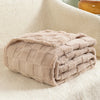 A folded light beige checkered fleece throw blanket resting on a white, fluffy surface.