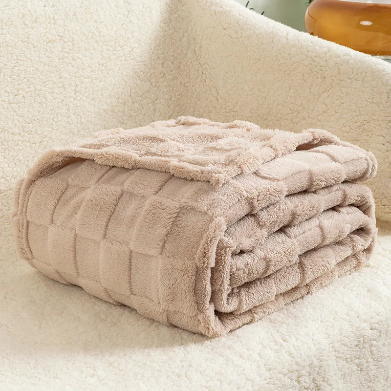 A folded light beige checkered fleece throw blanket resting on a white, fluffy surface.