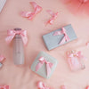 A collection of pink satin ribbon twist tie bows arranged on a light pink background with glass bottles.