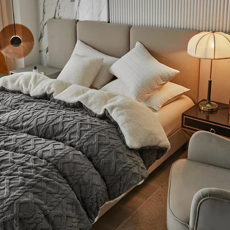 A cozy fleece blanket is draped over a light-colored bed with white pillows and a bedside lamp.