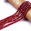 A strand of faceted, deep red glass beads is draped over a gold-colored cylindrical object.
