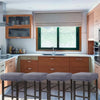 A row of four upholstered bar stools with gray slipcovers are positioned in front of a modern kitchen window.