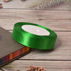 A roll of bright green satin ribbon with a white center is placed on a wooden surface next to a dark notebook.