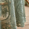 A sheer, sage green floral lace tablecloth with a tatting weave draped over a wooden table.