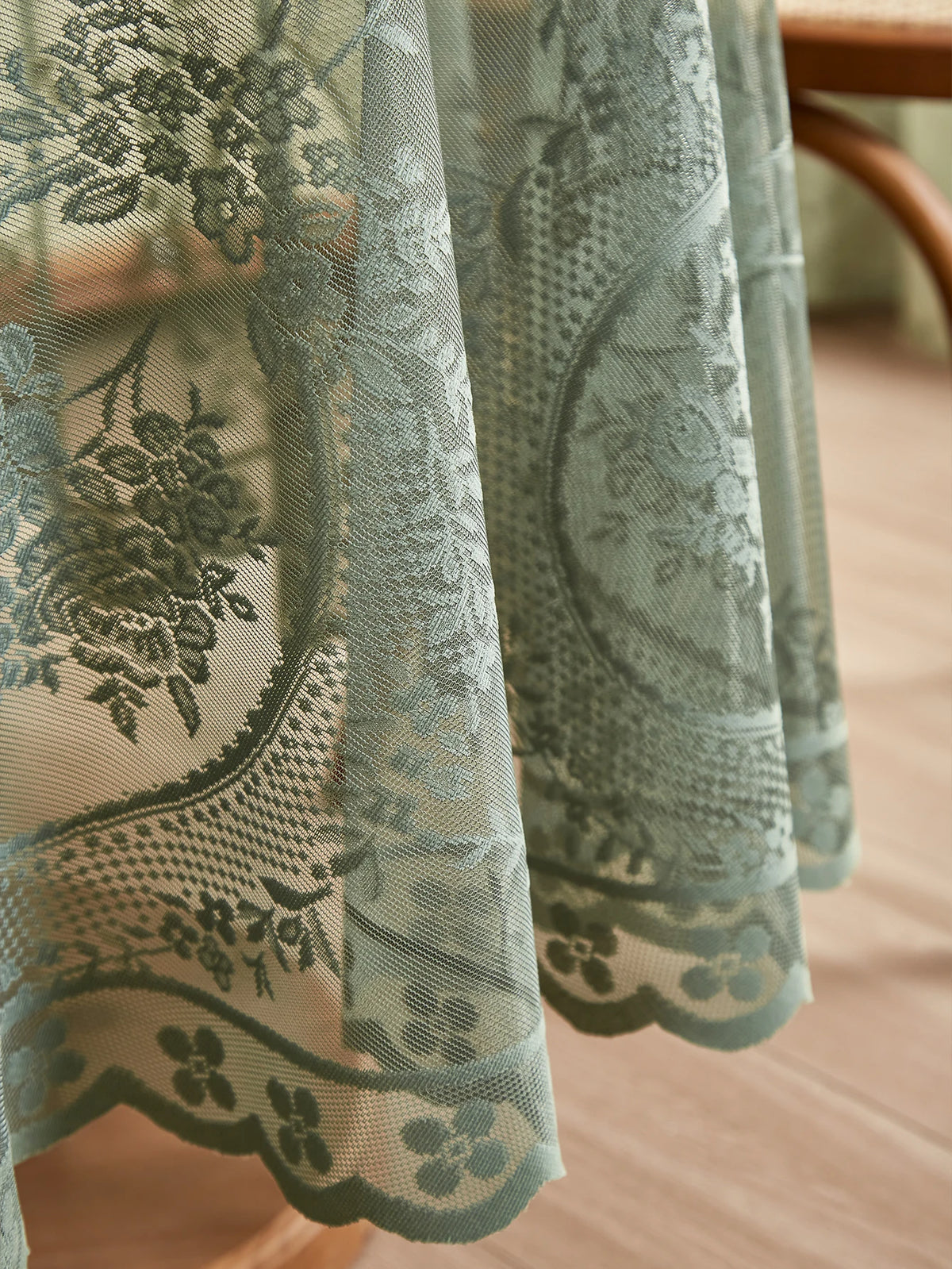 A sheer, sage green floral lace tablecloth with a tatting weave draped over a wooden table.