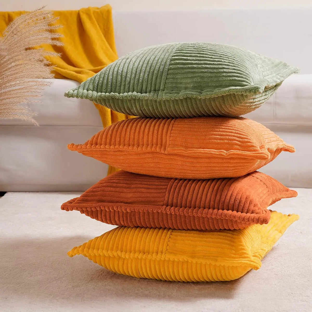A stack of three striped corduroy lumbar support pillows in shades of yellow, orange, and green on a light surface.
