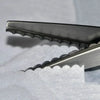 Close-up of professional dressmaking pinking shears with serrated edges resting on white fabric.