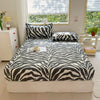 A bed with a zebra print fitted sheet and pillows in shades of gray and white.