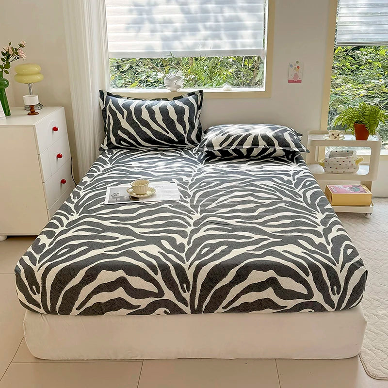 A bed with a zebra print fitted sheet and pillows in shades of gray and white.