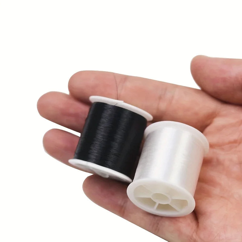 A hand holds a spool of black invisible nylon sewing thread and a spool of white invisible nylon sewing thread.