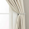 A close-up of a beige fabric curtain being held back by a silver metal curtain holdback hook.