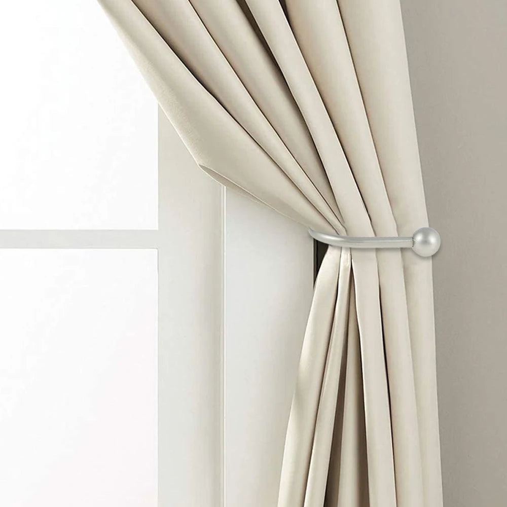 A close-up of a beige fabric curtain being held back by a silver metal curtain holdback hook.