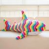 A colorful, striped giant shark plush toy lying on a light-colored sofa.