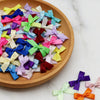 A collection of small satin ribbon bows in various pastel and jewel tones arranged on a wooden plate.