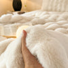 A hand is holding a fluffy white faux fur throw blanket on a bed.