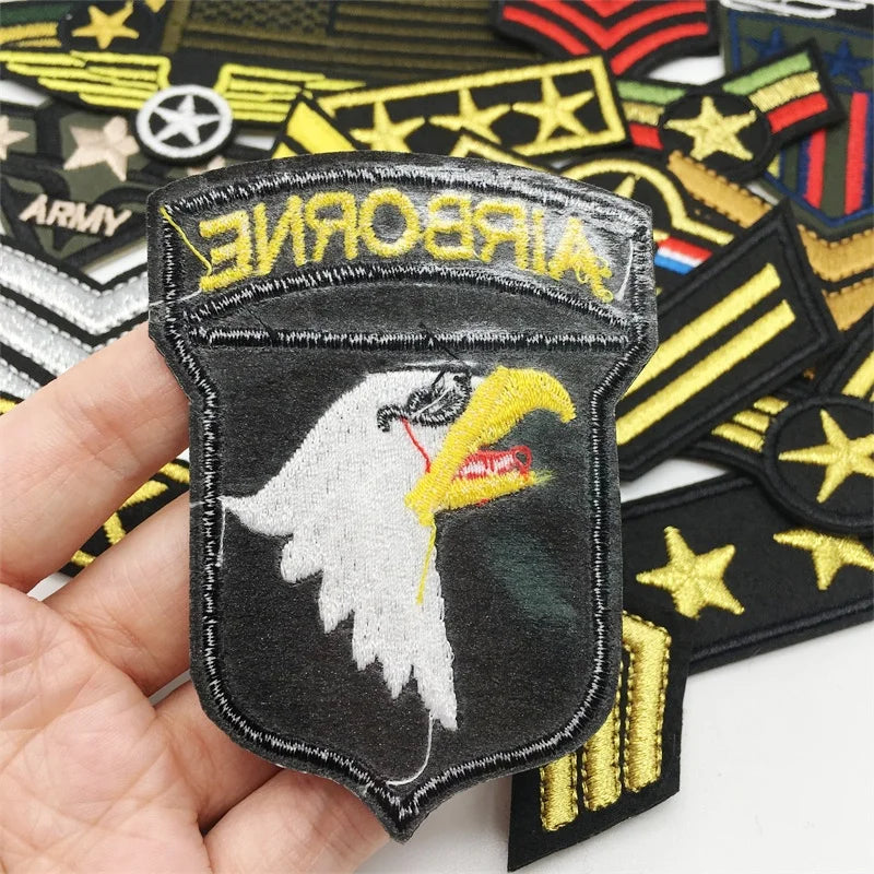 A hand holds an embroidered tactical clothing patch featuring a white eagle head on a black background.
