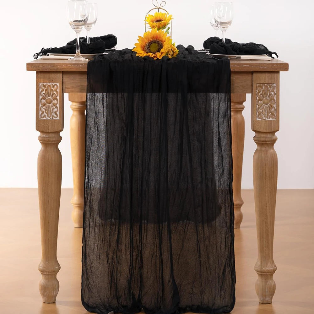 Black cheesecloth table runner draped over a wooden table with yellow flowers and glassware.