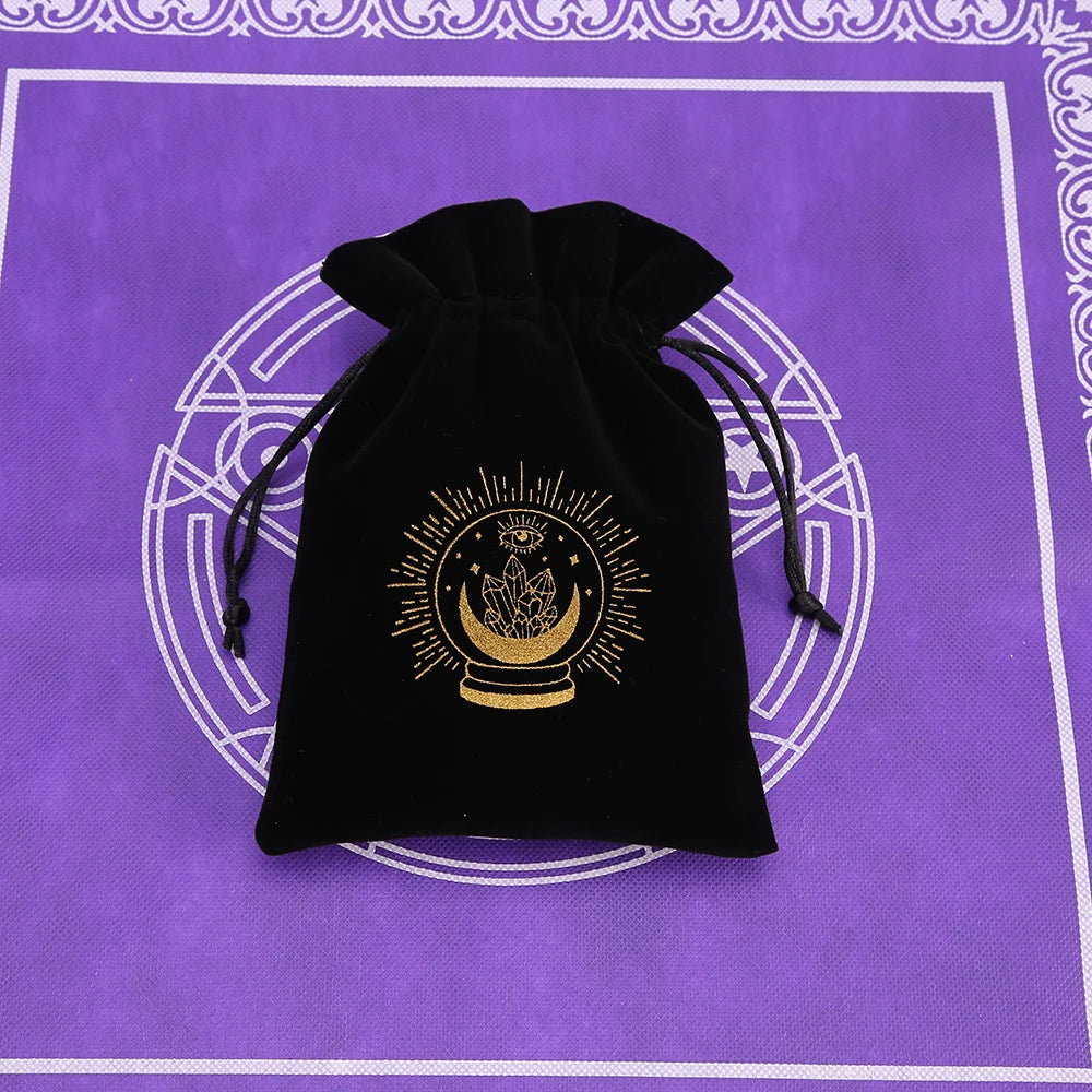 Black velvet pouch with a gold sun symbol embroidered on it, resting on a purple patterned surface.