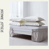 A white bed with an elegant ruffled skirt set featuring soft, light-colored linens and pillows.