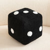 A black plush dice cube with white polka dots resting on a light surface.